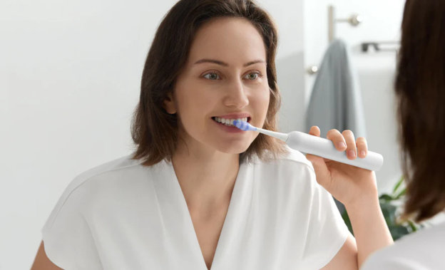 Woman brushing teeth with a smart electric toothbrush in a bright modern bathroom