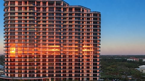 Sunset reflecting on glass facade of luxury waterfront tower with pools and terraces