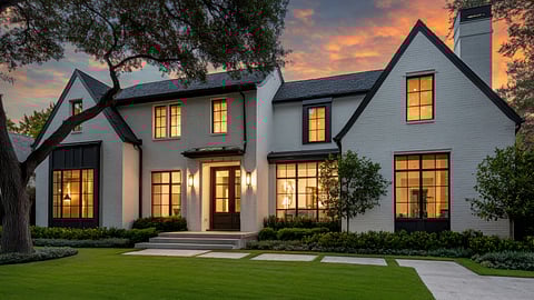 Modern white brick home with lit windows and landscaped lawn at sunset