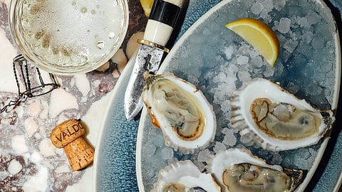 Oysters on ice with lemon, champagne, and oyster knife on marble table