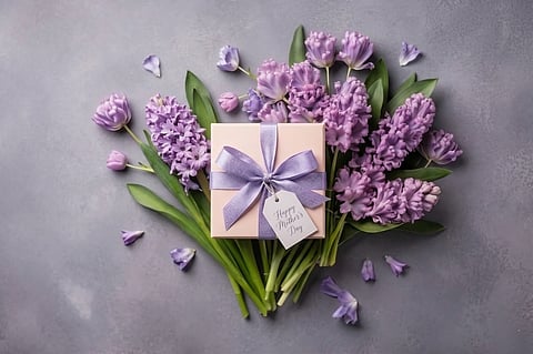 pink gift box with a purple ribbon and "Happy Mother's Day" tag, surrounded by purple hyacinths.