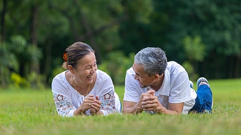 Senior couple lying on grass outdoors smiling and relaxing in a green park setting