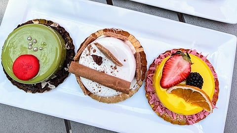 Three mini cakes with glossy glaze, fruit, and decorative toppings on white platter