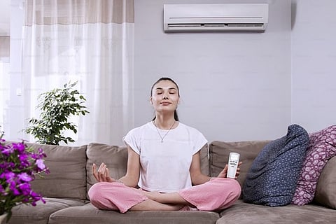A woman in a comfortable living room meditating with an HVAC unit in the background