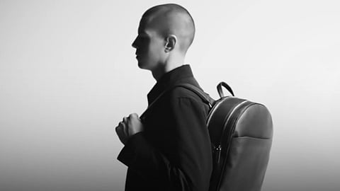 Montegrappa model in black carrying a leather backpack in a minimalist studio setting