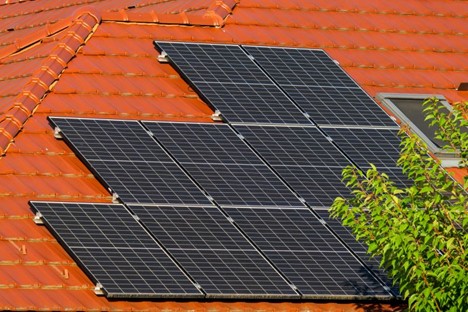 A residential solar panel array installed on a red-tiled roof