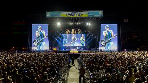 Country artist performing on large festival stage with crowd at night and bright concert screens