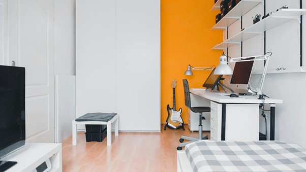 A minimalist student room with a striking orange accent wall
