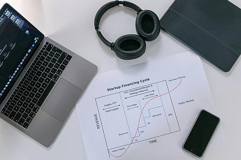 a workspace arranged with a laptop, wireless headphones, and documents
