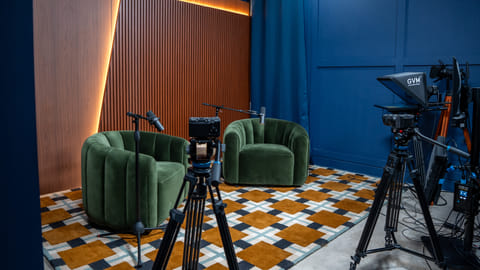 Podcast studio with green chairs, cameras, and microphones set for recording