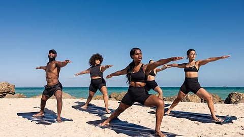 Group practicing yoga poses on mats along the beach at The Miami Beach EDITION
