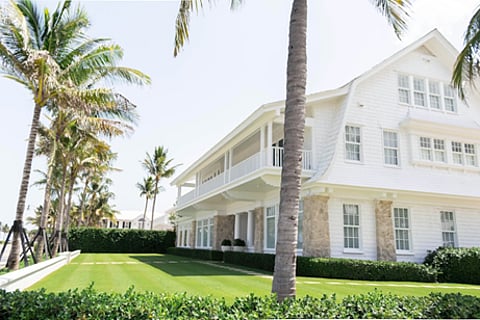 a white, multi-story villa with palm trees and a landscaped lawn