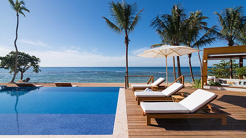 Infinity pool with lounge chairs overlooking ocean and palm trees