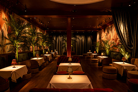 Dimly lit dining room at Le Bar Penelope with velvet seating, table lamps, and lush greenery