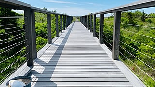A scenic elevated boardwalk beneath a bright blue Hamptons sky