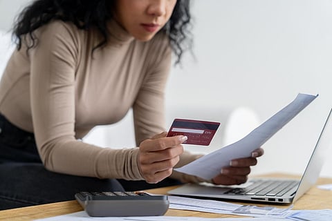 a person's hands holding a red credit card and a white paper document while using a laptop computer