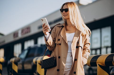 a photo of a young woman in a beige trench coat holding a smartphone