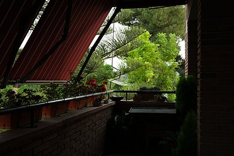 a cozy balcony featuring a red and white striped awning for shade and various potted plants