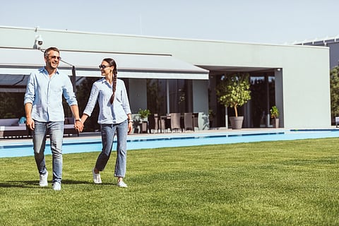 a couple walking on a lawn near a modern house with a pool