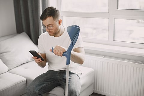 a person seated on a white sofa, holding a forearm crutch