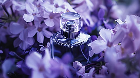 Perfume bottle nestled among purple flowers with a soft-focus floral background