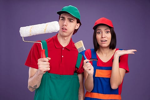 two individuals holding a paint roller and brush