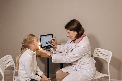 a pediatrician using a small flashlight to check a young girl's throat
