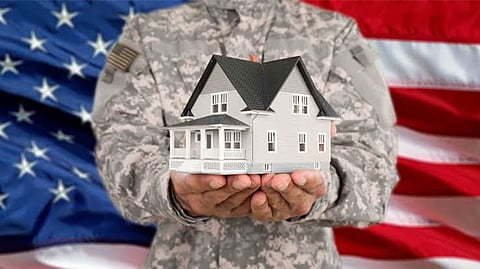 Person in military camouflage uniform holding a small model house