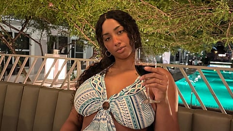 Person sitting by a pool holding a glass of wine at night