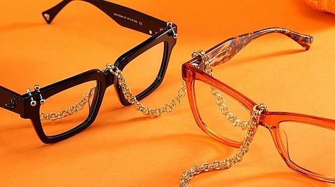 Stylish black and orange eyeglasses with gold chains on an orange background.