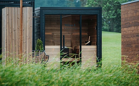 Modern outdoor sauna cabin with glass doors in a green garden.