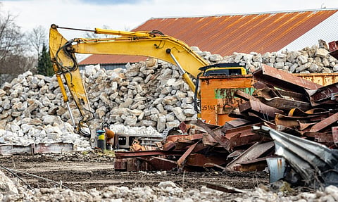 Excavator working among rubble and scrap metal at a demolition site.