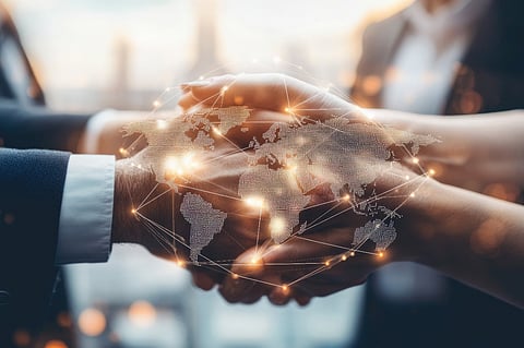 Business professionals joining hands beneath a glowing digital world map.