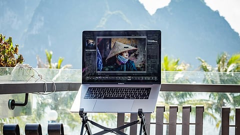 A laptop sits on a table, with a scenic view of mountains in the background.