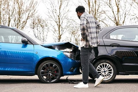 A man stands beside a damaged car, assessing the collision's impact on the vehicle's exterior.
