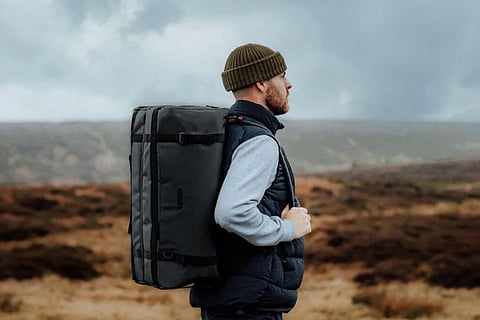 A man with a backpack stands in a grassy field