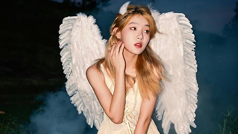 A woman with white wings sits gracefully on the grass