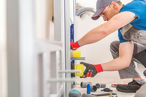 Worker wearing safety gloves repairing or installing a door frame with tools in an indoor setting.