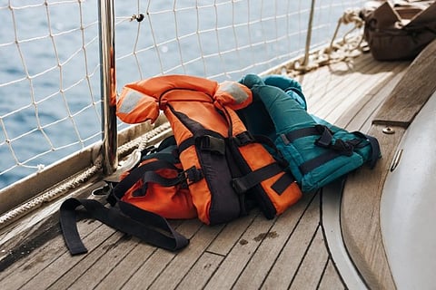 Orange and teal life jackets placed on the deck of a boat near the water.