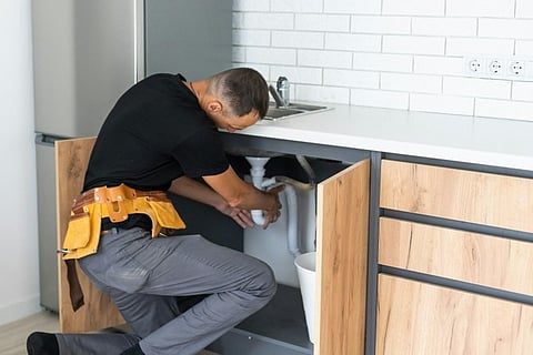Plumber repairing pipes under a kitchen sink cabinet in a modern home.