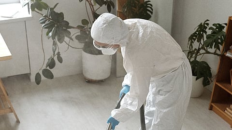 Person wearing protective suit cleaning a carpet with a steam machine indoors.