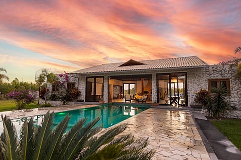 Stone villa with a swimming pool and garden under a colorful sunset sky.