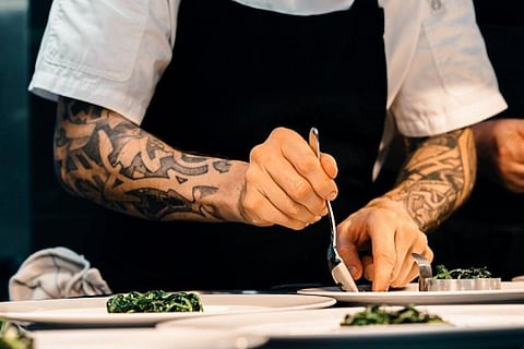 Tattooed chef plating food.