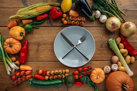 Empty plate with cutlery surrounded by fresh vegetables.