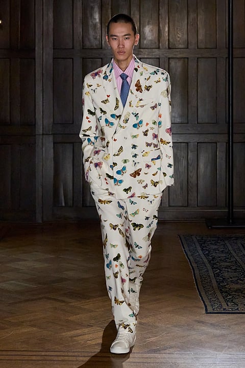 Model in an ivory suit printed with butterflies in a wood-paneled room