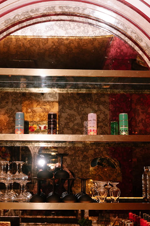 A mirrored bar with an arched ceiling, stacked glassware and colorful cocktail cans on the shelves