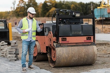 Construction worker standing next to a road roller.