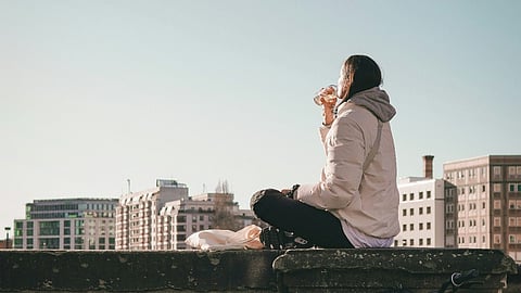 Woman sitting on a wall drinking above a bicycle.