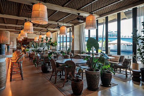Open dining room at CASA NEOS with woven pendant lights, plants and a view of the Miami River