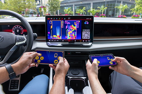 Two passengers use smartphones as game controllers while a block puzzle game